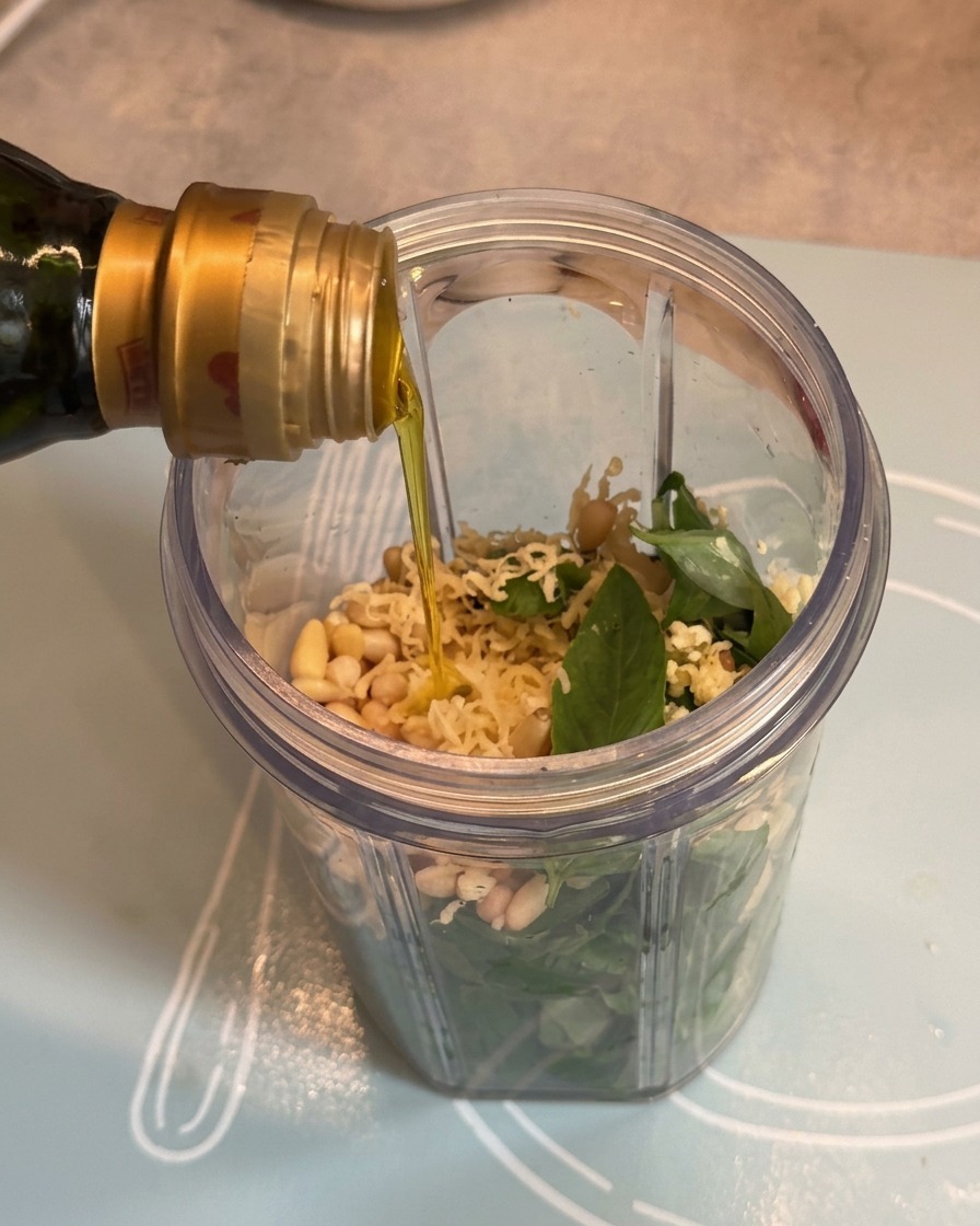 Oliwa z oliwek wlewana z butelki do kubka blendera nad składnikami pesto.