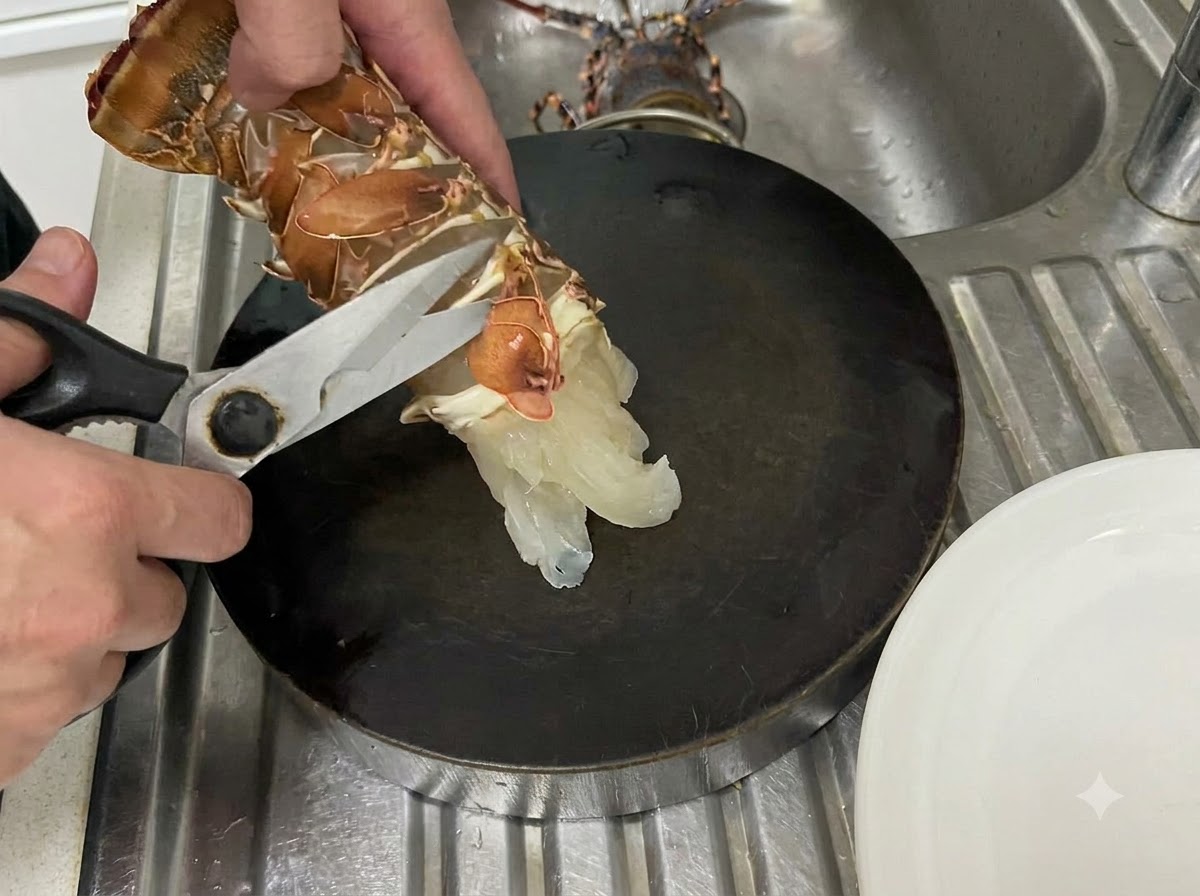 Ręce używające nożyczek kuchennych do cięcia wzdłuż dolnej błony surowego ogona langusta nad ciemną deską do krojenia.
