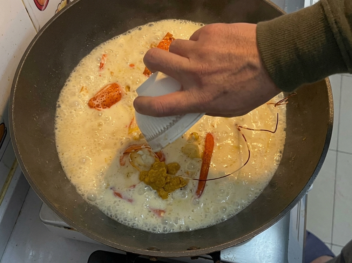 Odkładana żółta pasta z langusta wlewana z małej białej miseczki do woka ze smażonymi kawałkami langusta i kremowym sosem.