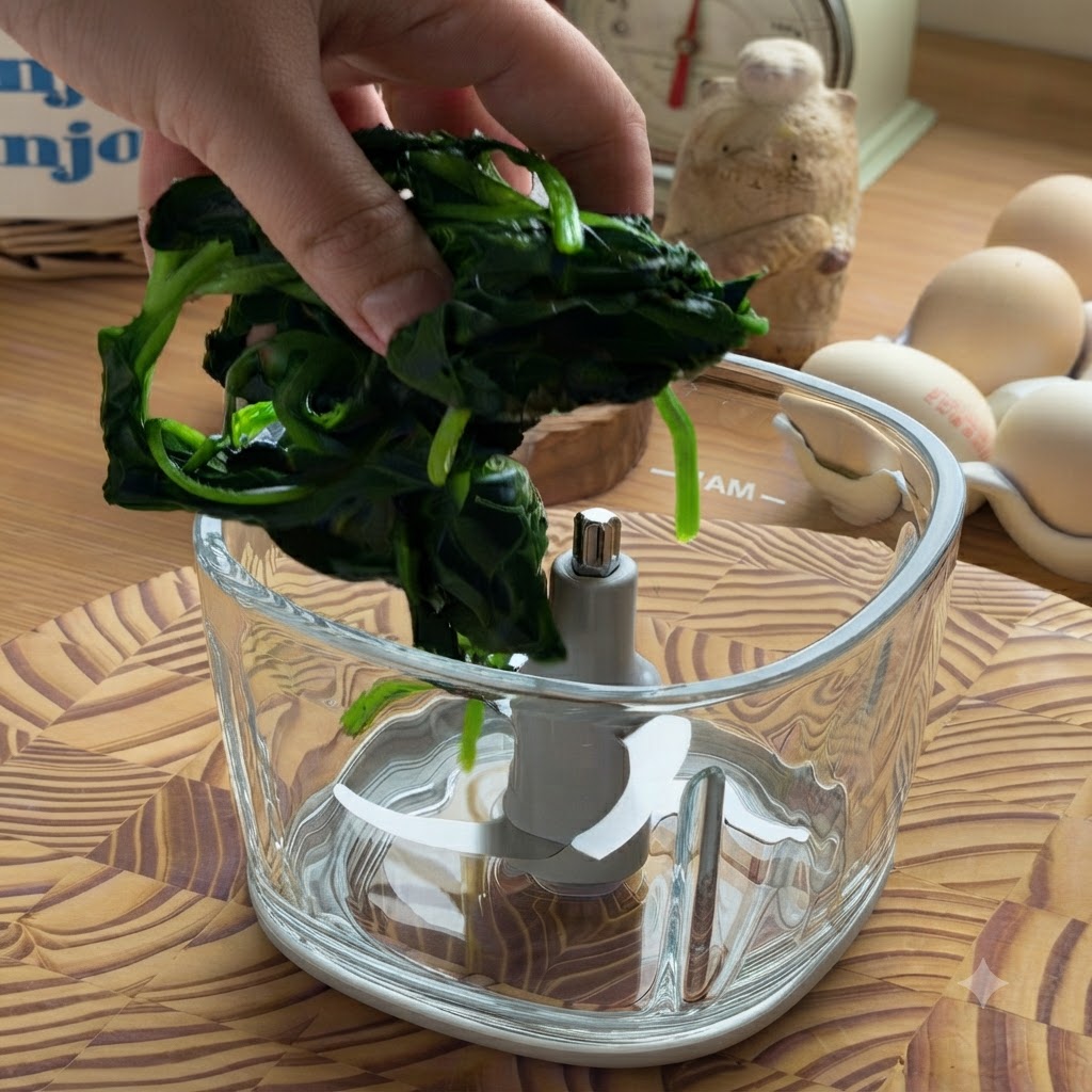 Ręka umieszczająca kępkę odciśniętego, ugotowanego szpinaku w pustej szklanej misce robota kuchennego.