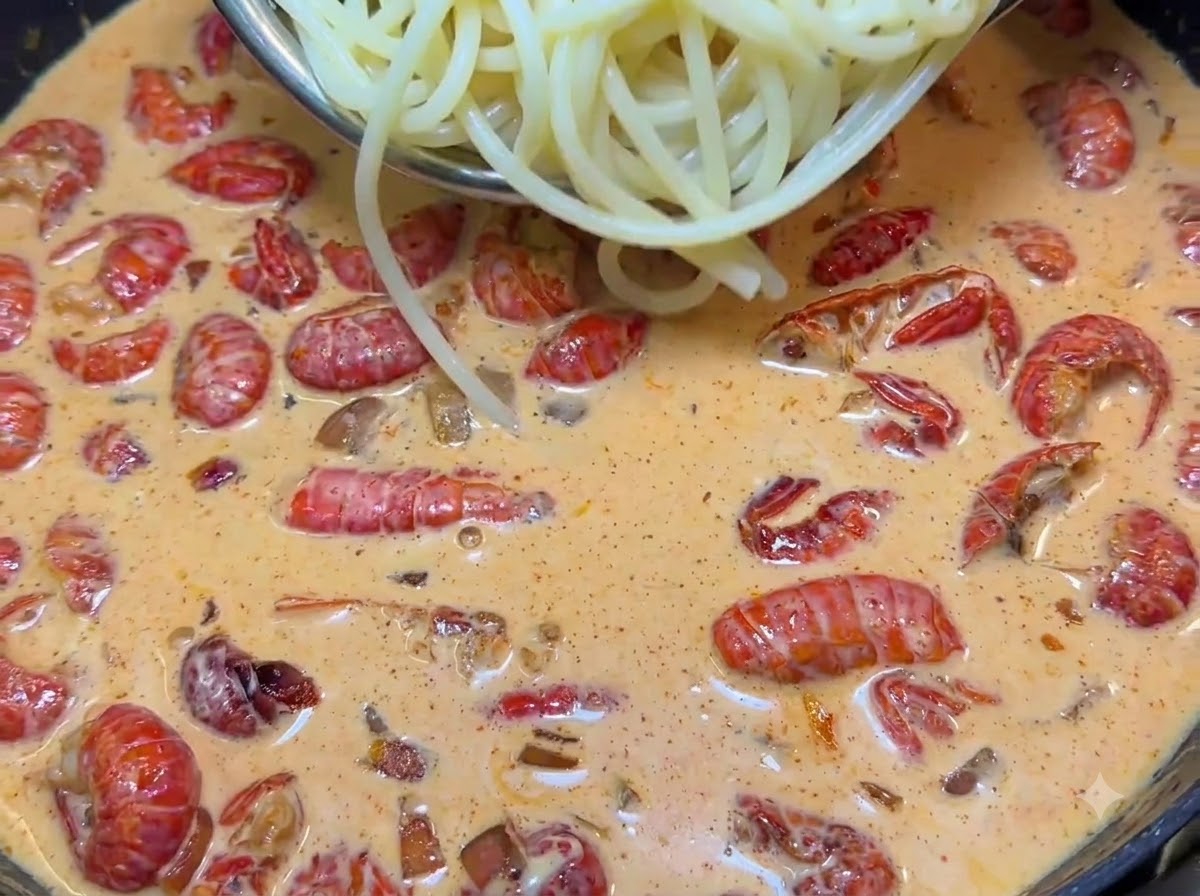 Szczypce przenoszące ugotowany makaron spaghetti na patelnię z kremowym sosem i rakami.