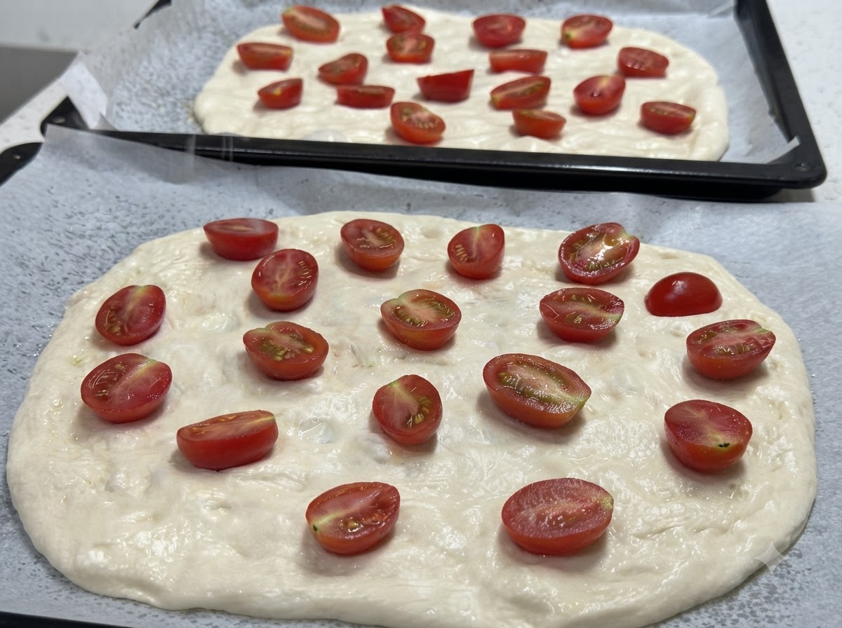 Zbliżenie na dwa rozciągnięte spody do pizzy posypane połówkami pomidorków koktajlowych, gotowe do doprawienia.