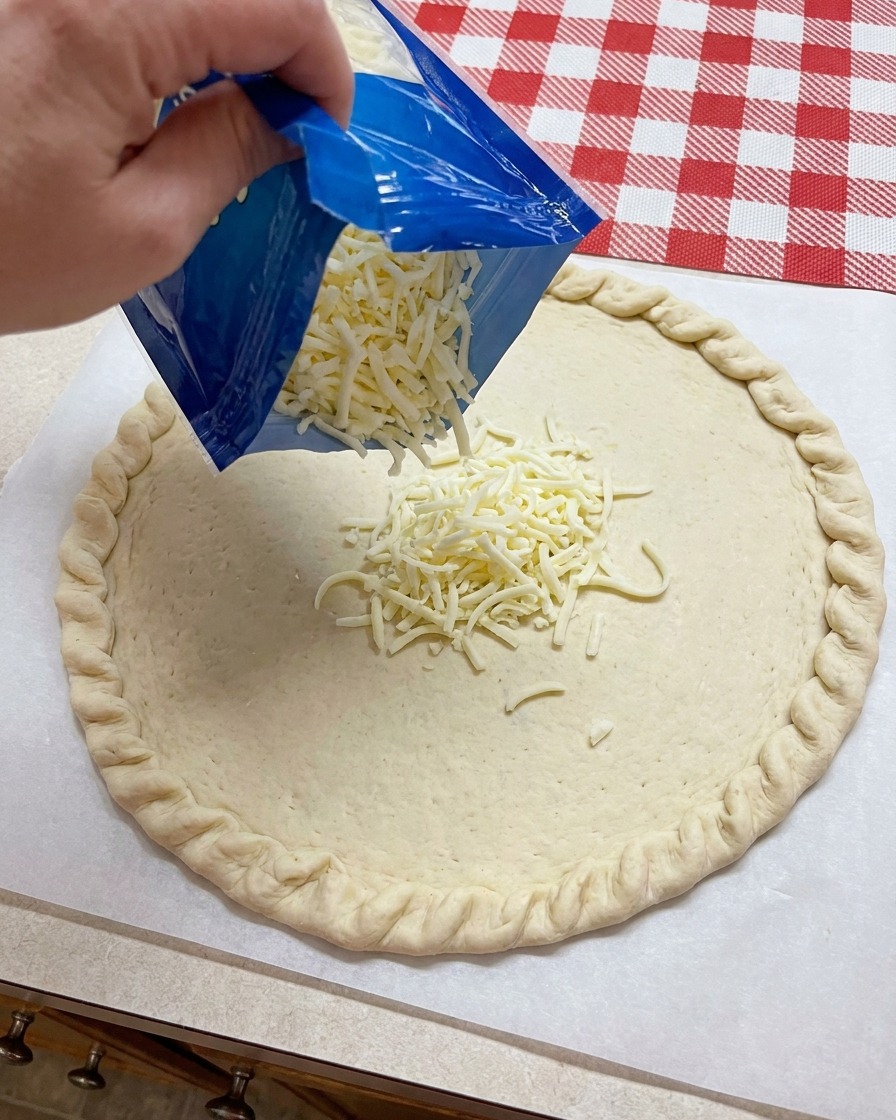 Tarta mozzarella sypana z niebieskiego opakowania na środek uformowanego spodu do pizzy.