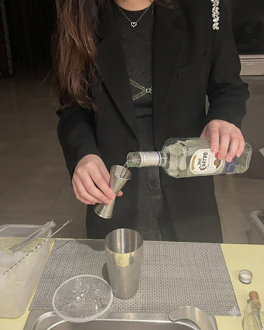Tequila nalewana z butelki do miarki barmańskiej umieszczonej nad metalowym shakerem.