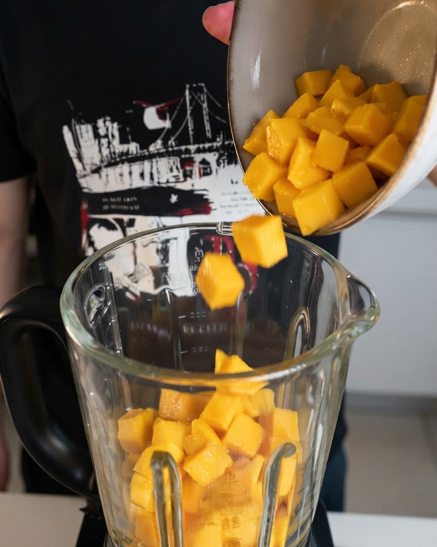 Świeżo pokrojone żółte kostki mango wsypywane z miski do dzbana blendera.