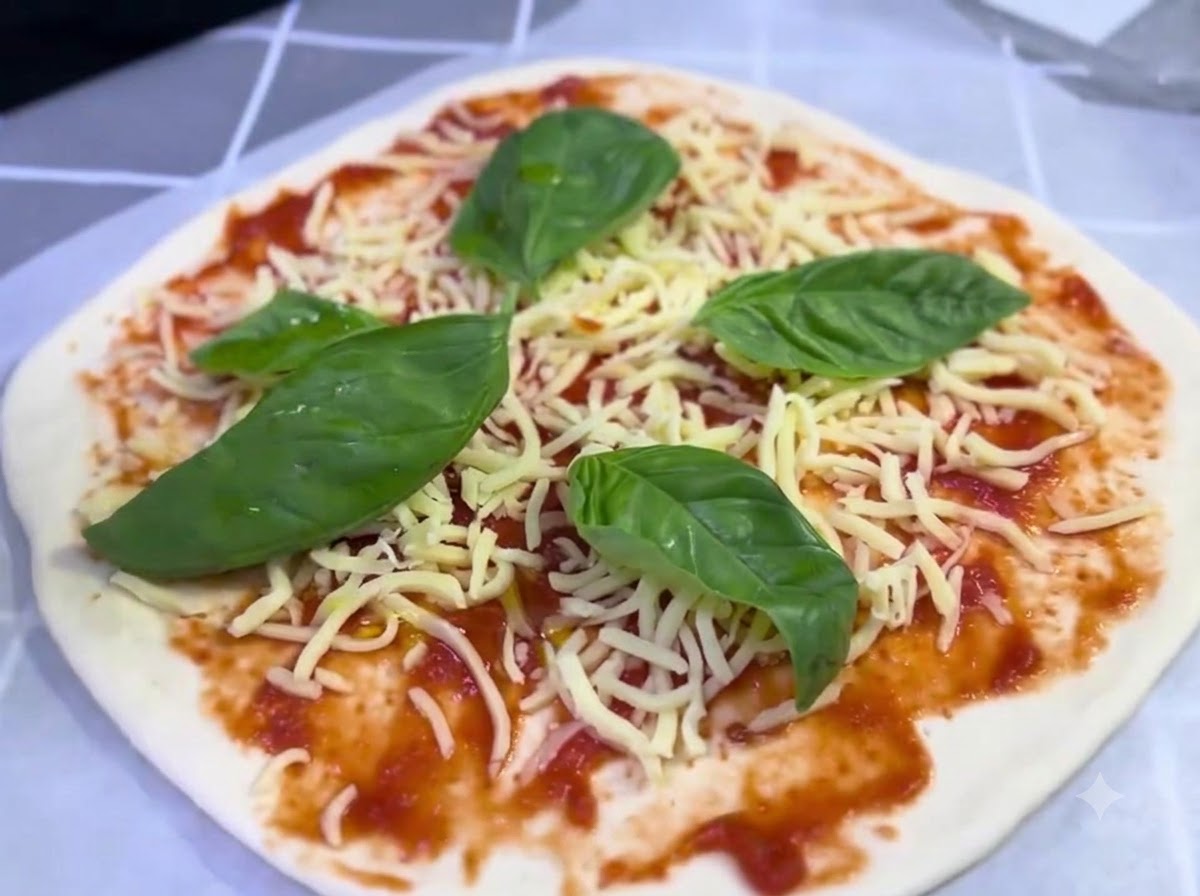 Złożona pizza z dodatkiem sera i liści bazylii otrzymująca lekki strumyk oliwy z oliwek.