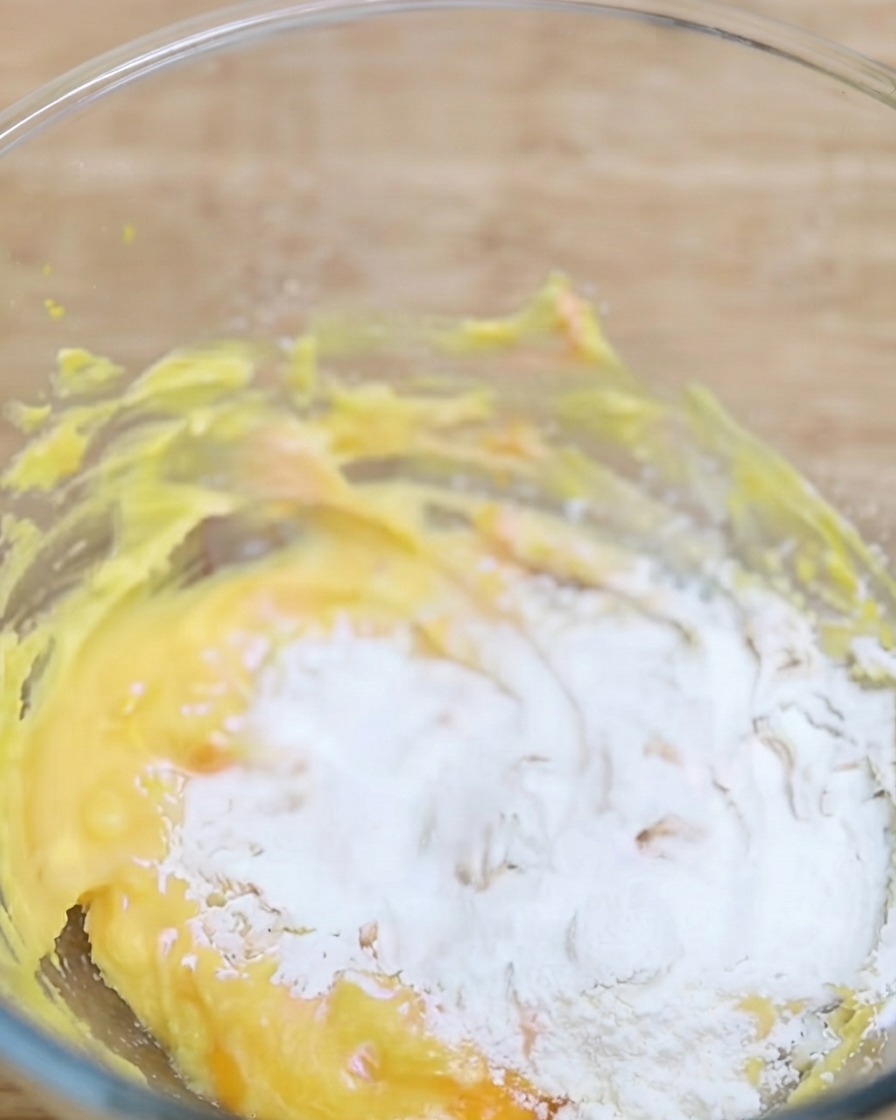 Proszek matcha przesiewany do miski zawierającej żółtą bazę ciasta.