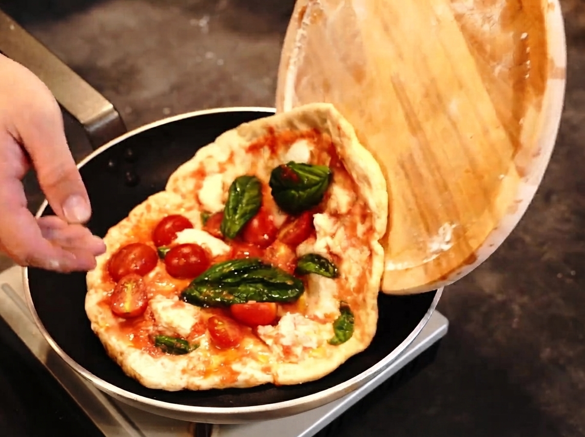 Pizza przekładana z drewnianej łopaty na patelnię, podczas gdy w pobliżu przygotowany jest palnik kuchenny.