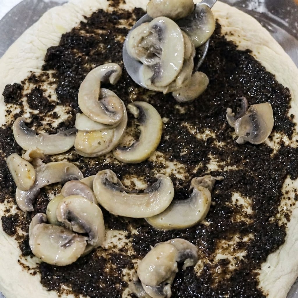 Łyżka układająca plasterki ugotowanych grzybów na spód pizzy pokryty pastą z czarnych trufli.