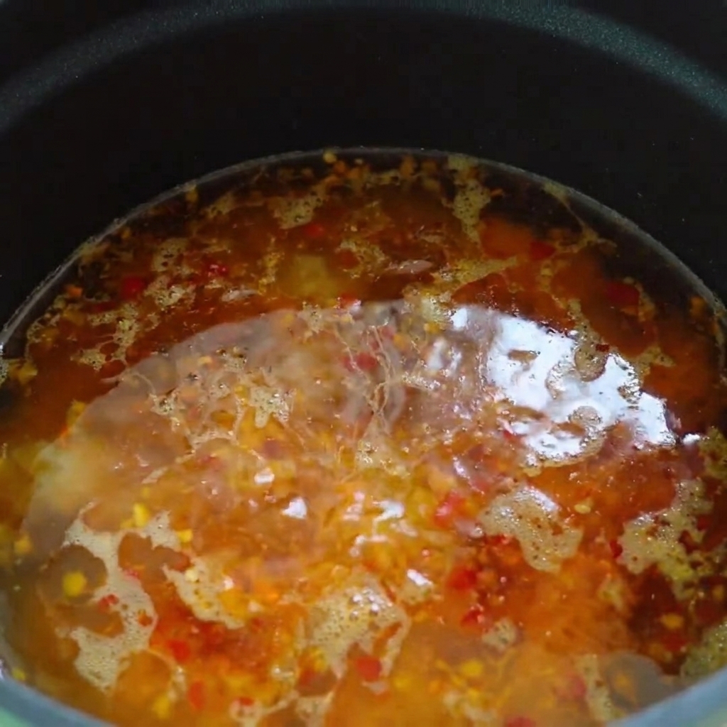 Olej chili i olej sezamowy skrapiane po powierzchni gorącej bazy zupy.