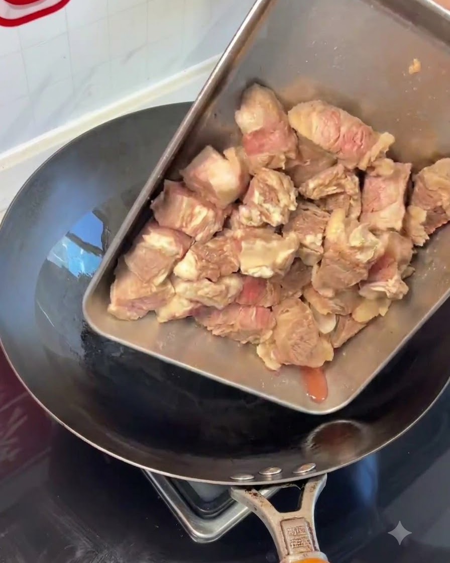 Kawałki zblanszowanych żeberek wołowych przekładane ze stalowej tacy do gorącego woka.