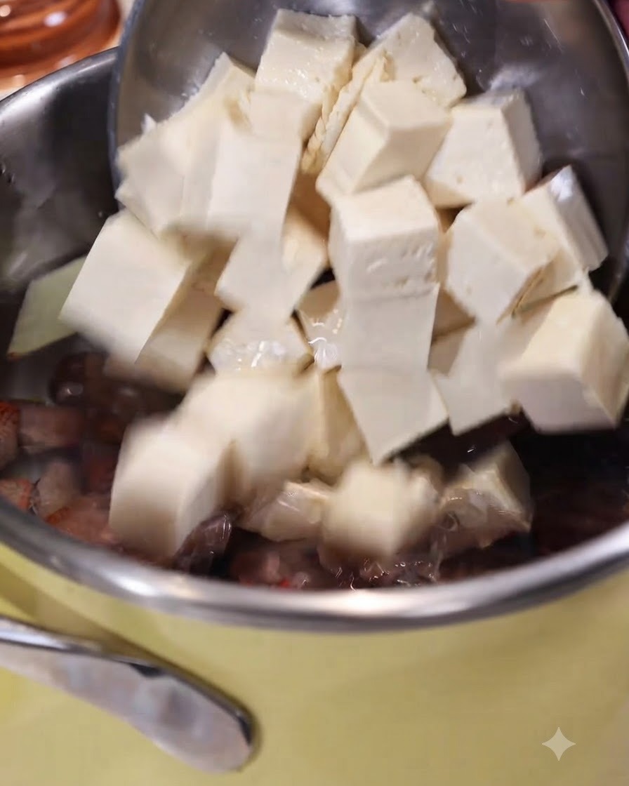 Pokrojone w kostkę tofu zsuwane z łyżki cedzakowej do garnka z wrzącą wodą z imbirem i małżami.