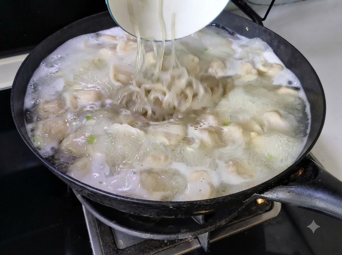 Makaron wsypywany z białej miski do bulgoczącej zupy z pierogami w woku.