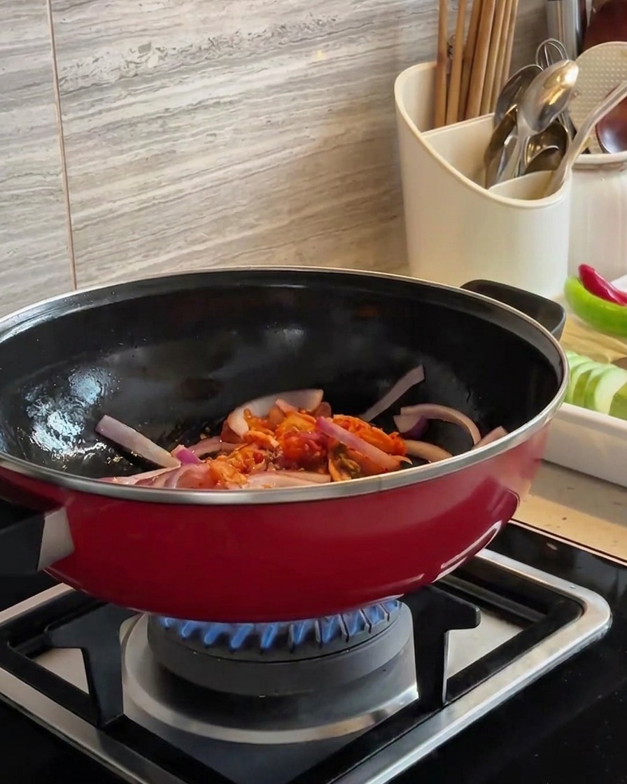 Plastry czerwonej cebuli i posiekane kimchi podsmażane razem w czerwonym woku nad niebieskim płomieniem.