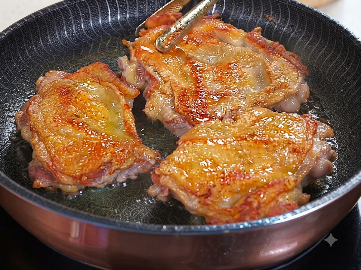Trzy zrumienione na złoto udka z kurczaka skwierczące na patelni podczas polewania sosem teriyaki.