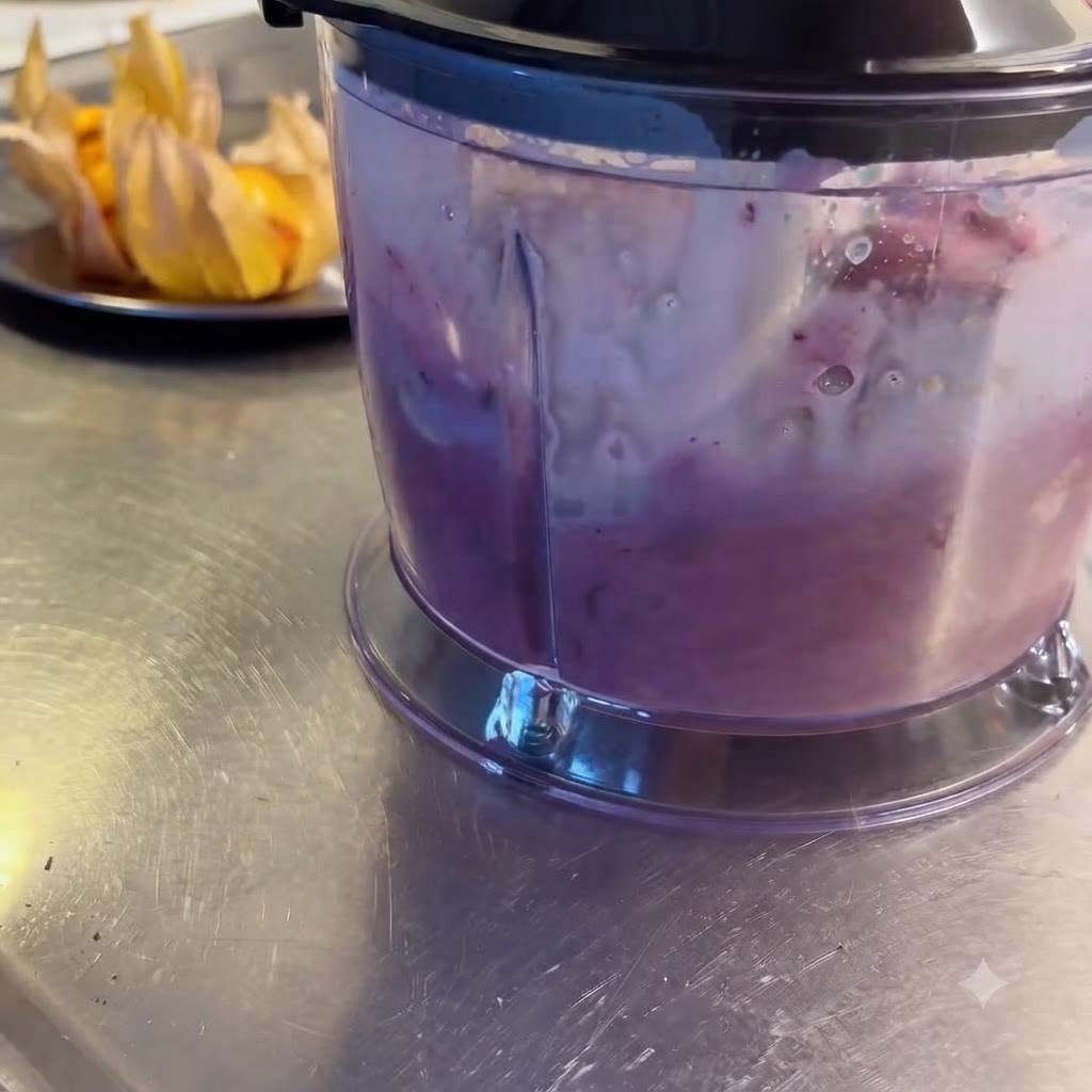 Blender miksujący owoce leśne, miechunkę i mleko na gładki, fioletowy napój.