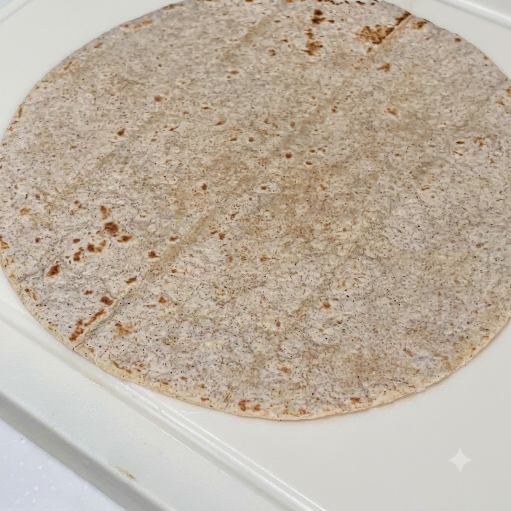 Tortilla pełnoziarnista posmarowana sosem z masła orzechowego, z ułożonym kurczakiem, czerwoną kapustą i świeżą sałatą.