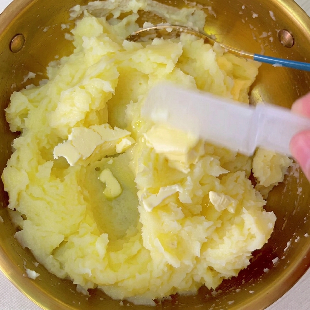 Kawałki masła mieszane w misce z ciepłym puree ziemniaczanym.