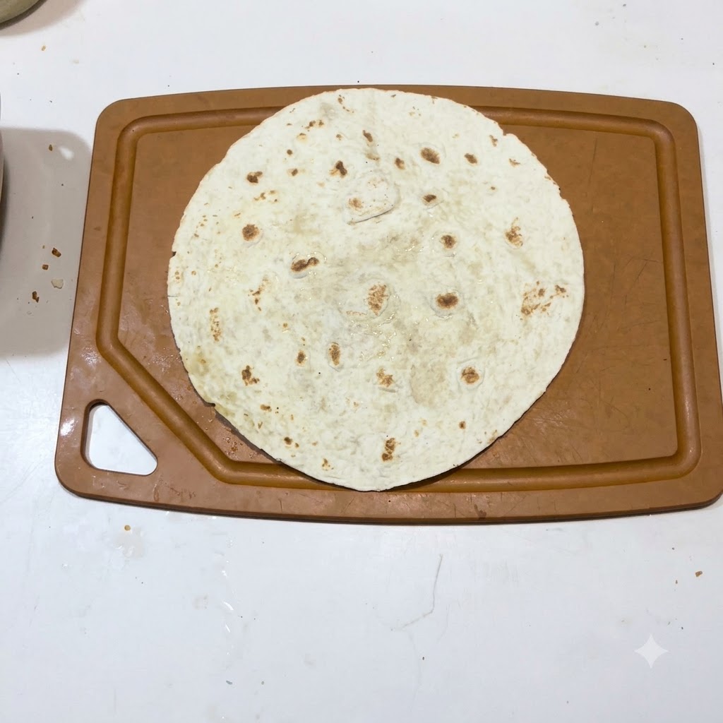 Pojedyncza ciepła tortilla ułożona płasko na brązowej desce do krojenia.