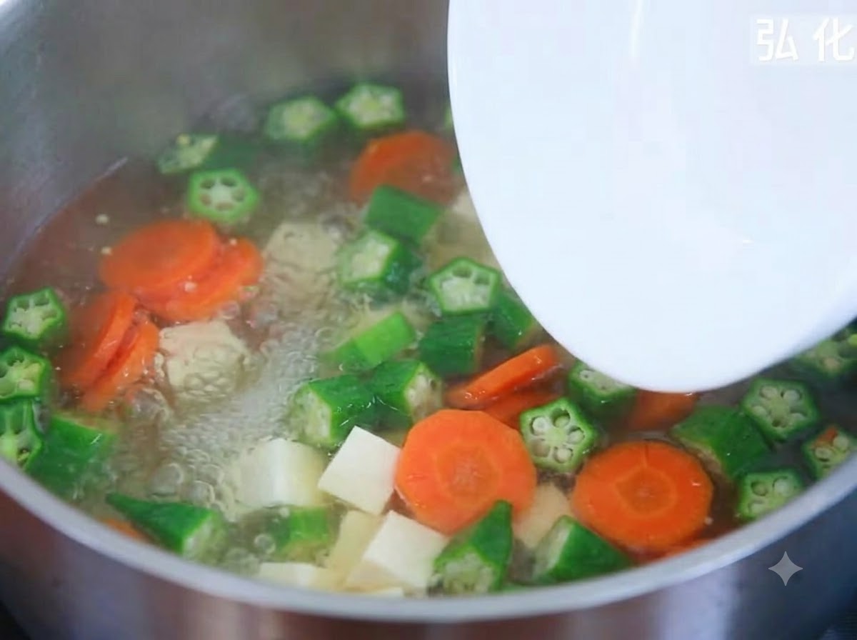 Kostki miękkiego tofu dodawane z talerza do bulgoczącego garnka z zupą warzywną.
