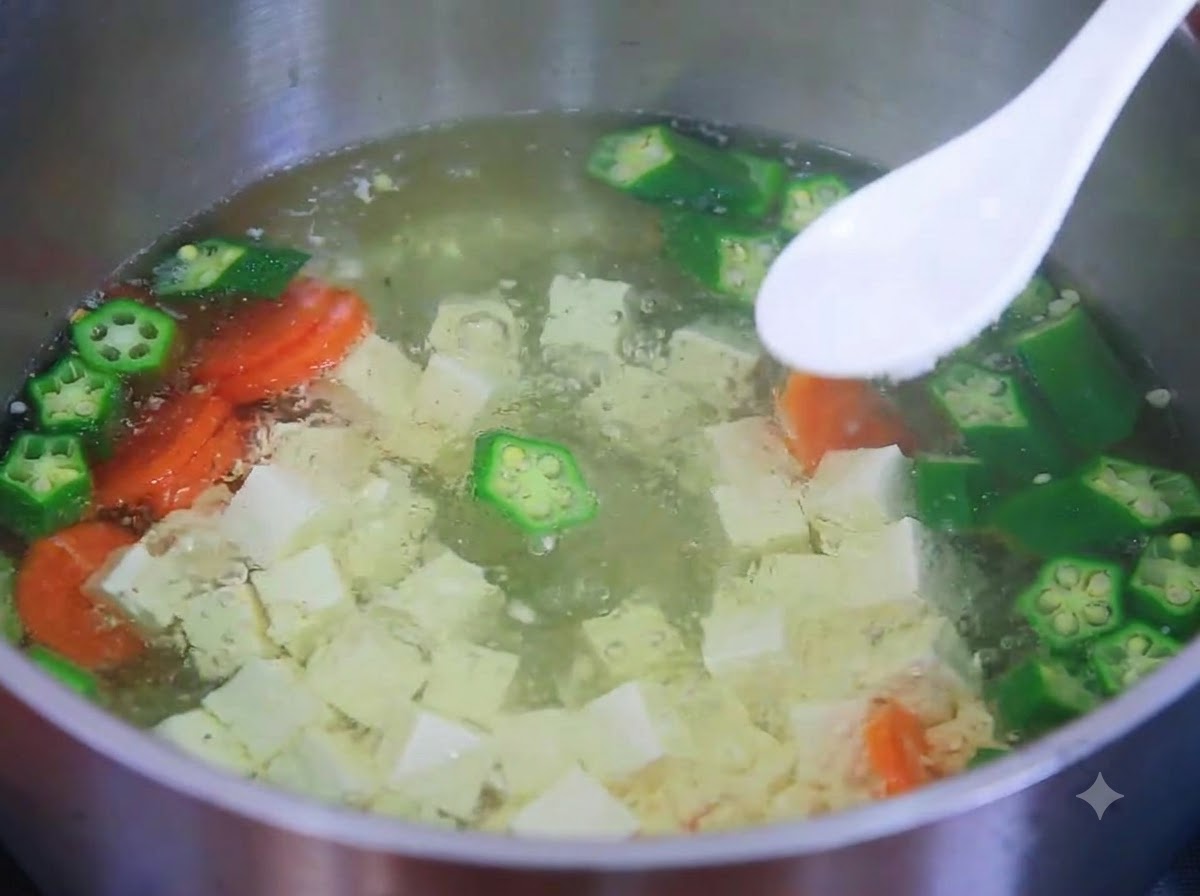 Biała łyżka trzymająca sól nad gotującą się zupą z tofu, okry i marchewki.