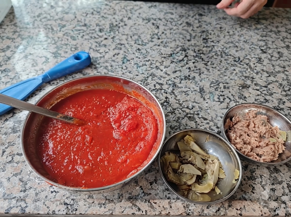 Cztery stalowe miski ze składnikami na pizzę ustawione na marmurowym blacie.