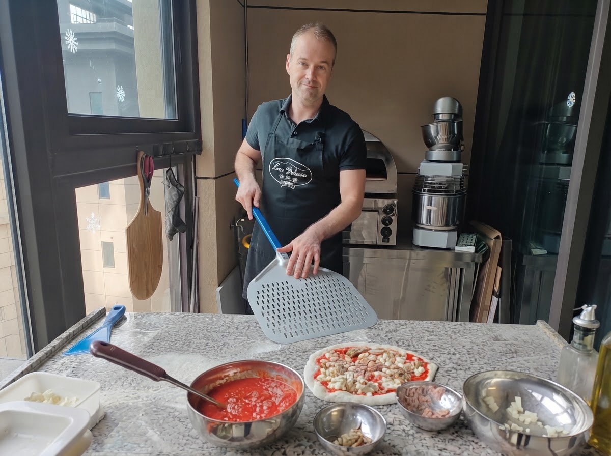 Pizzaiolo trzymający dużą, perforowaną metalową łopatę tuż obok przygotowanej, surowej pizzy.