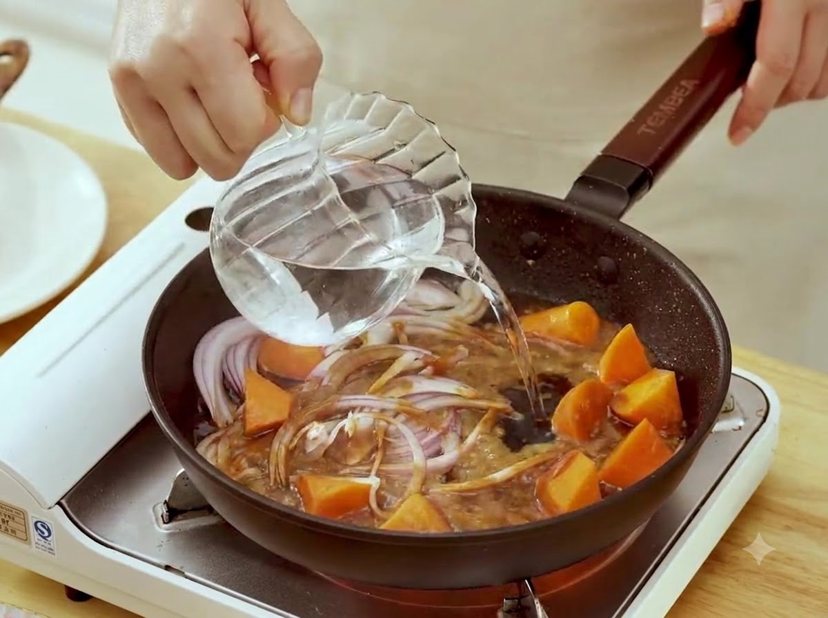 Woda wlewana ze szklanego dzbanka na patelnię z pokrojoną czerwoną cebulą i kawałkami marchewki w sosie miso.