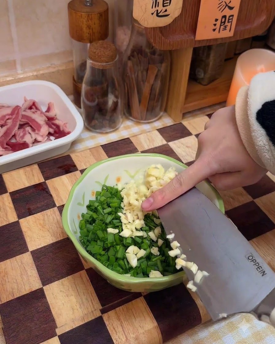 Posiekany czosnek dodawany do miski z posiekaną zieloną cebulką i przyprawami.