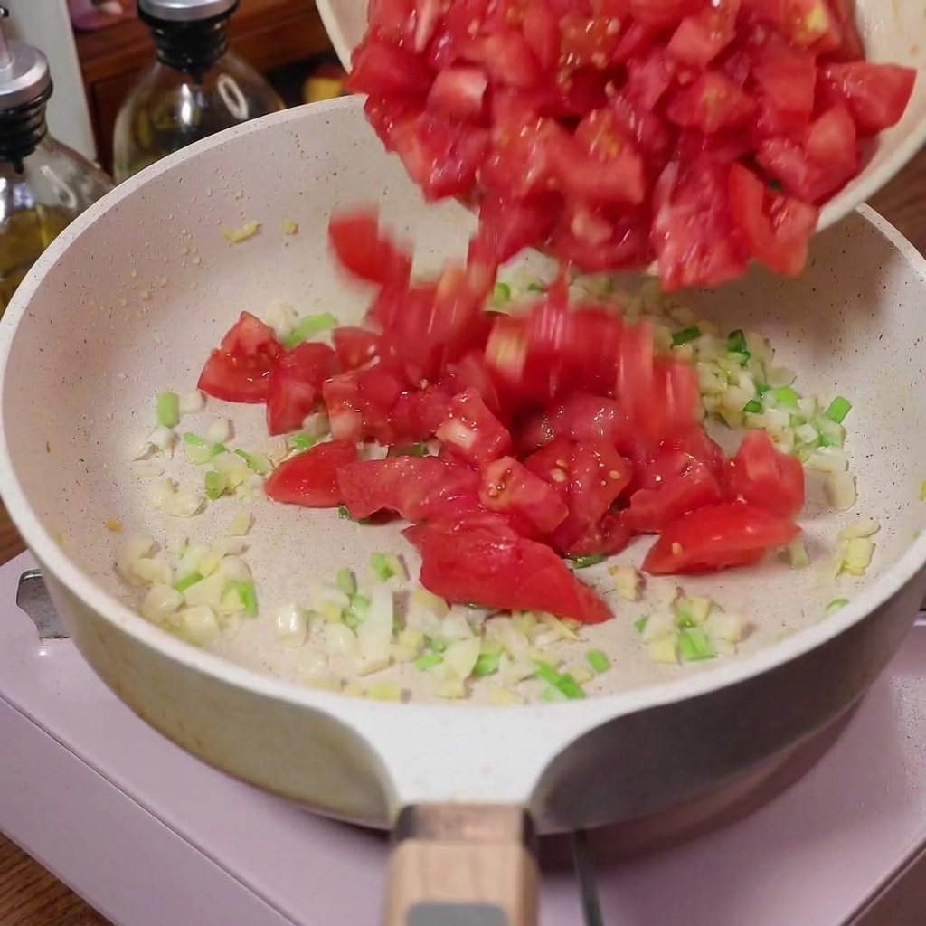 Pokrojone w kostkę pomidory wsypywane na patelnię z podsmażonymi aromatyчними składnikami.