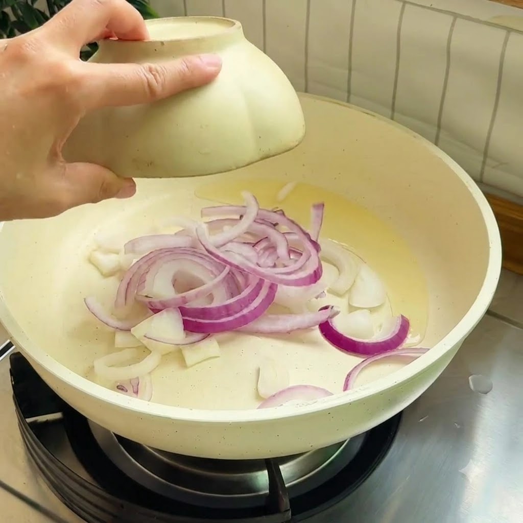Paski czerwonej cebuli smażone na rozgrzanej patelni z olejem.