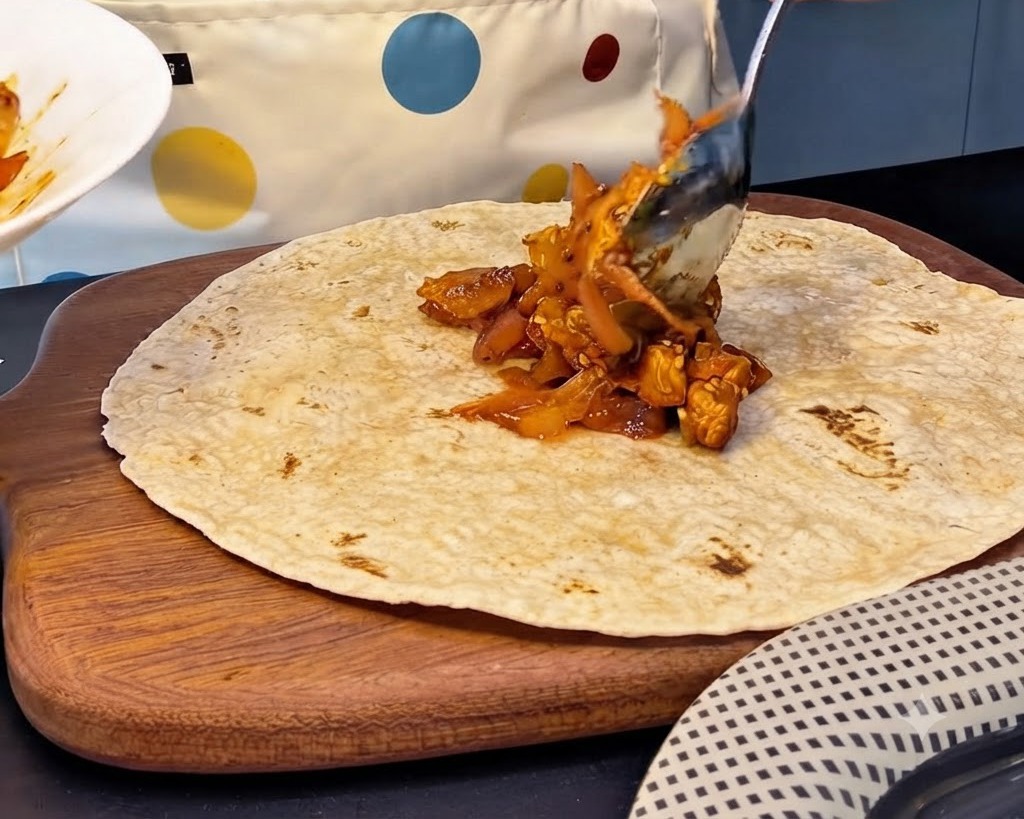 Duża łyżka pikantnego farszu z kurczaka i kimchi nakładana na środek pełnoziarnistej tortilli.
