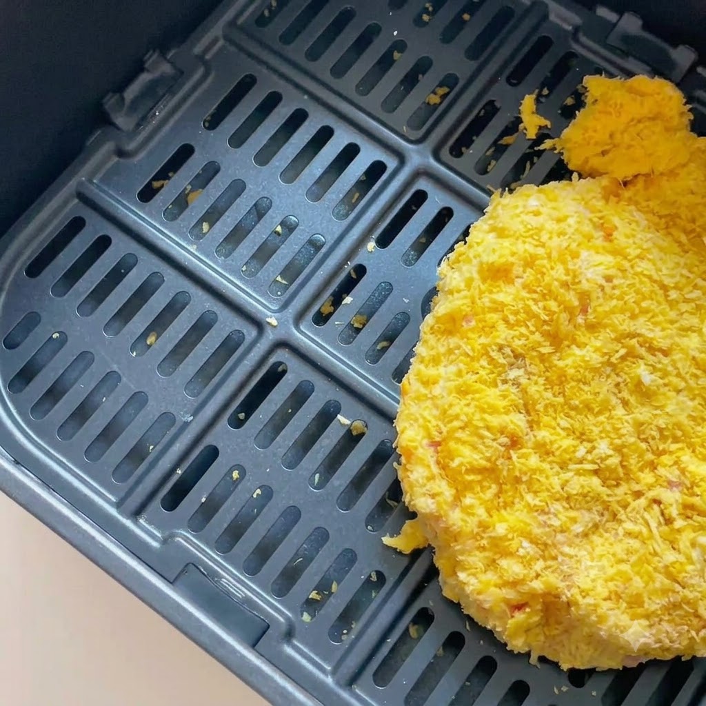 Panierowany kotlet wieprzowy leżący w koszu ciemnej frytkownicy powietrznej.