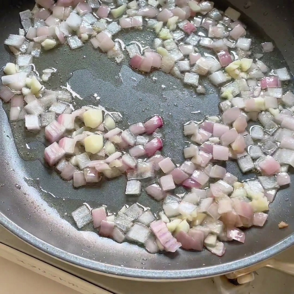 Pasta curry dodana do patelni zawierającej podsmażoną cebulę i czosnek, mieszana razem.