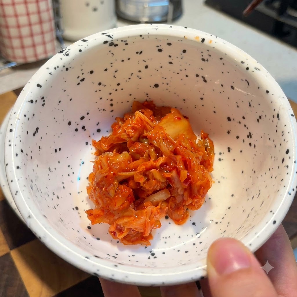 Biała nakrapiana miska wypełniona porcją jasnoczerwonego posiekanego kimchi.