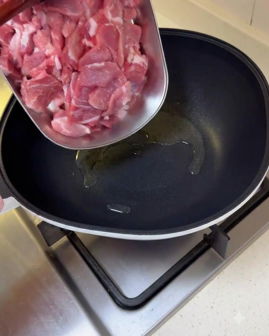 Surowe, cienkie plastry wieprzowiny przenoszone z tacy na naoliwioną patelnię.