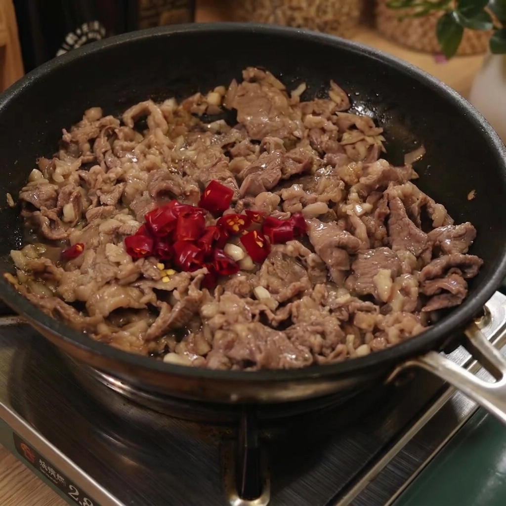 Ugotowany makaron spaghetti dodawany na patelnię z wołowiną i pokrojonymi czerwonymi papryczkami chili.