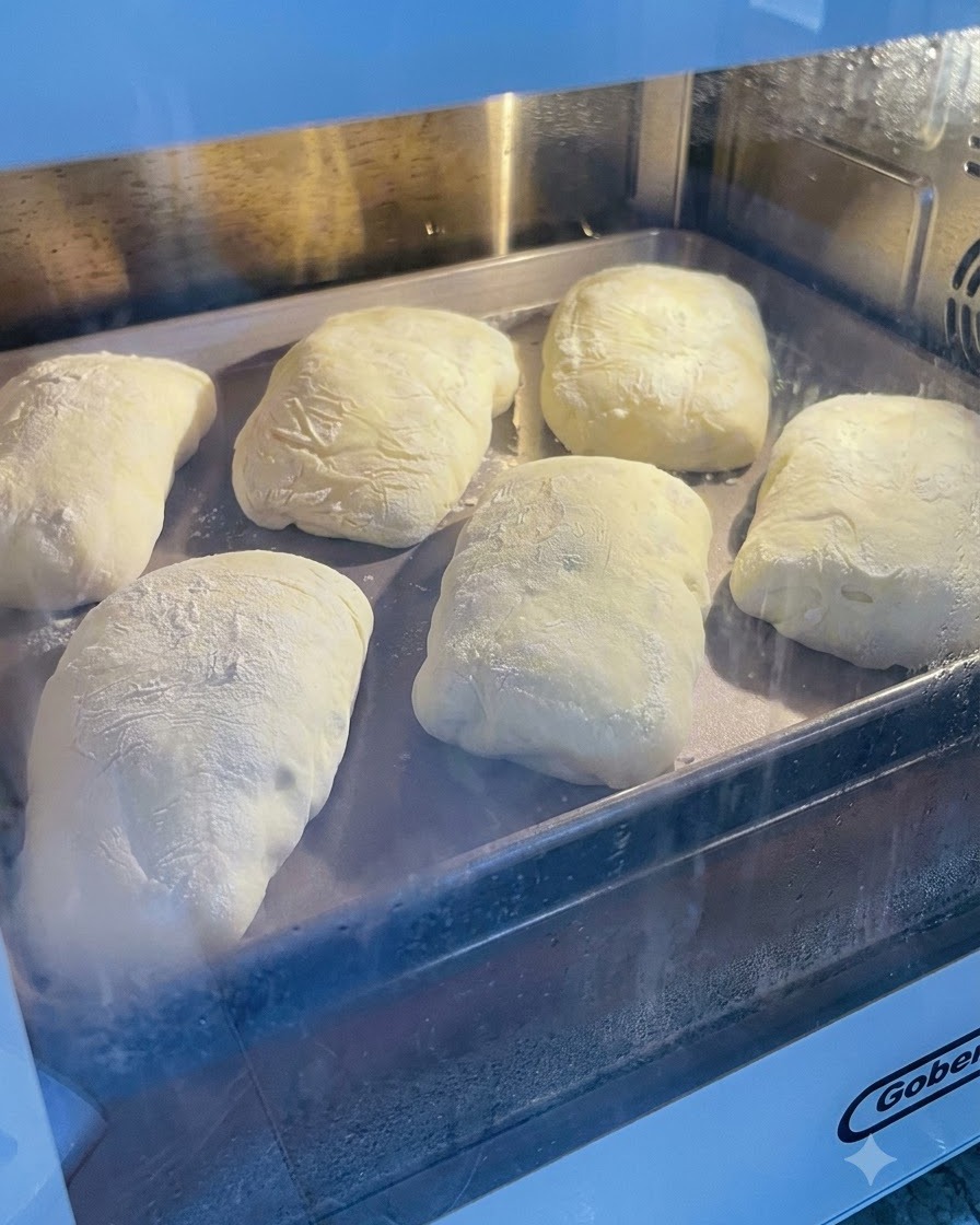 Sfermentowane ciasto oprószone mąką siedzące na metalowej blasze do pieczenia wewnątrz piekarnika.