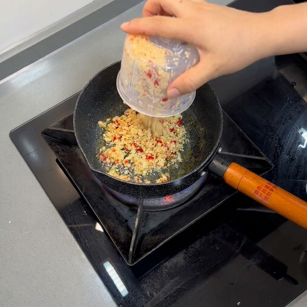 Posiekany czosnek i czerwona papryczka chili smażą się na rozgrzanym oleju na małej patelni.