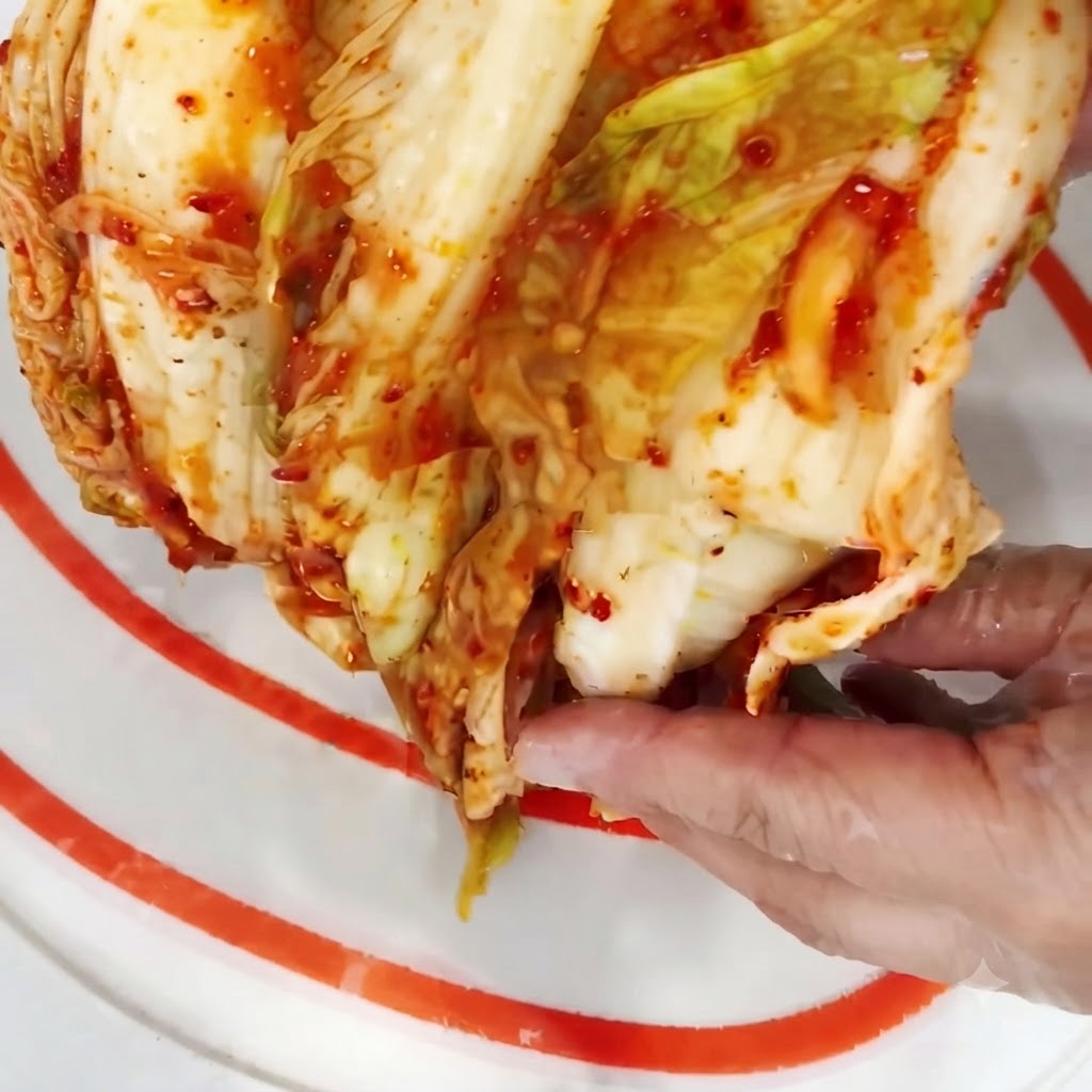 Połowa główki kimchi krojenita na mniejsze kawałki na desce do krojenia.