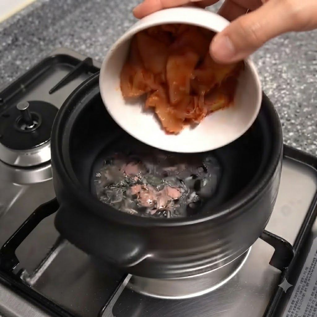 Biała miska pochylająca się i wsypująca posiekane czerwone kawałki kimchi do czarnego glinianego garnka.