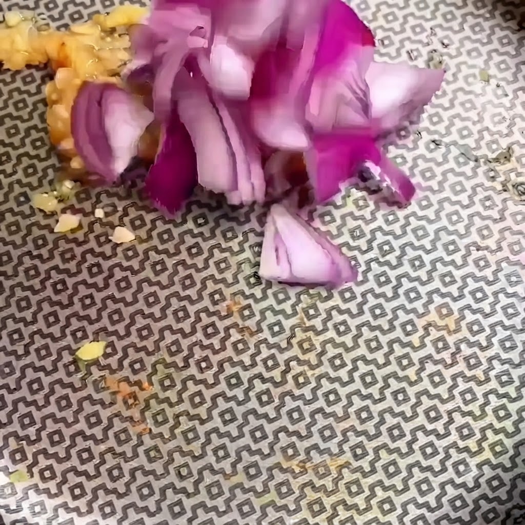 Kawałki posiekanej czerwonej cebuli dodawane do posiekanego czosnku na wzorzystej patelni.