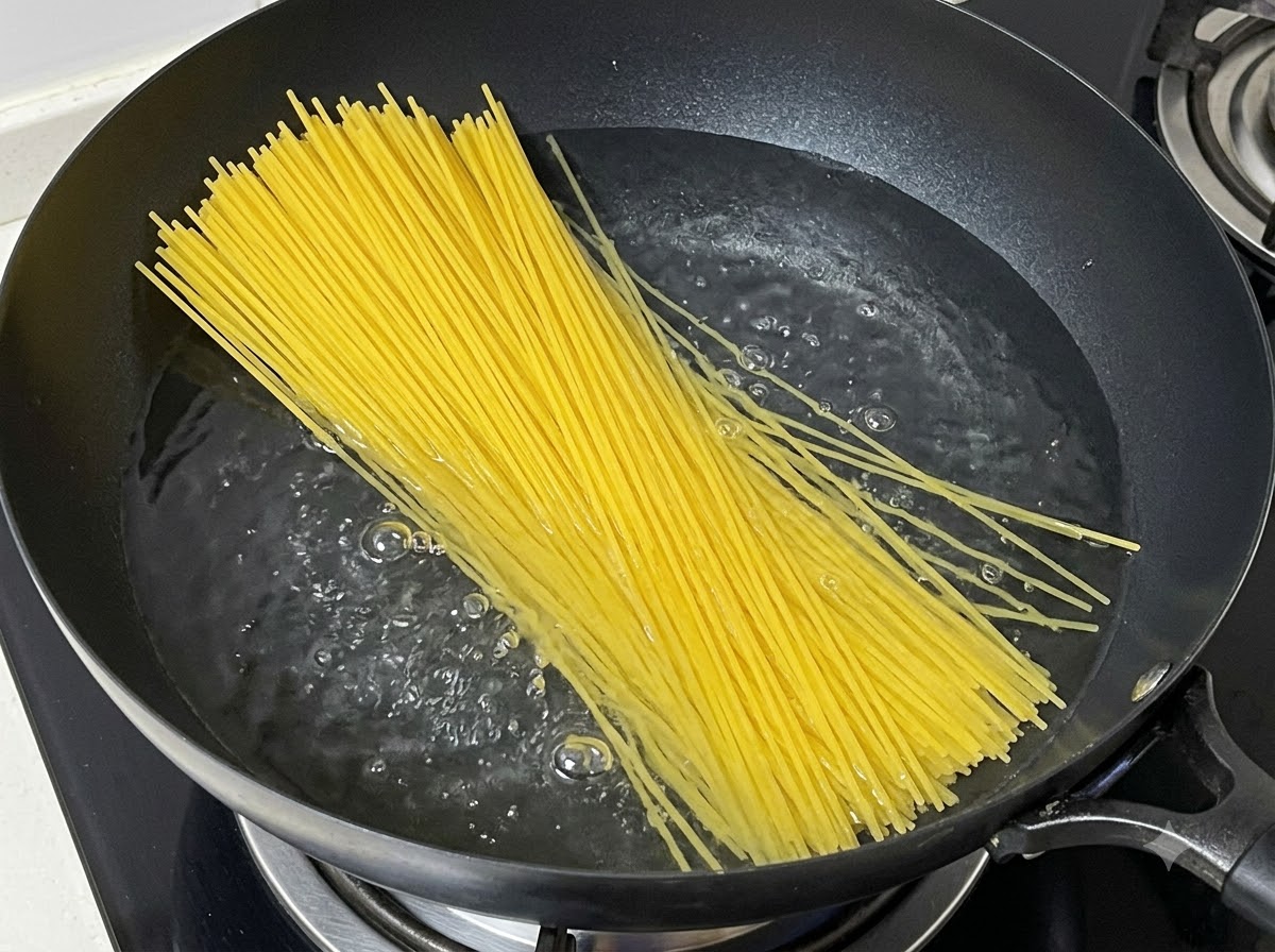 Wiązka suchego makaronu spaghetti wkładana do garnka z wrzącą wodą.