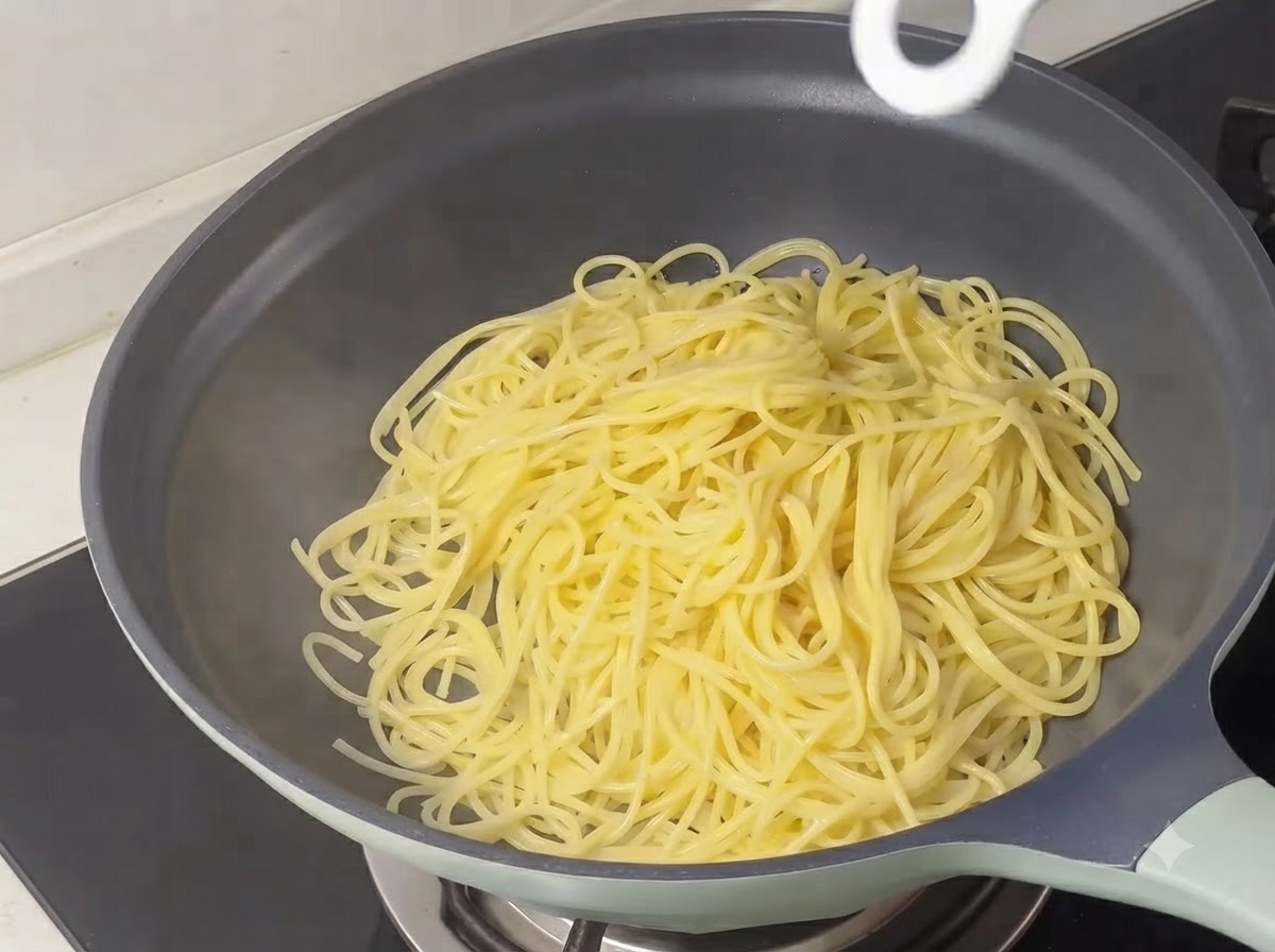 Ugotowane żółte nitki spaghetti ułożone na patelni.