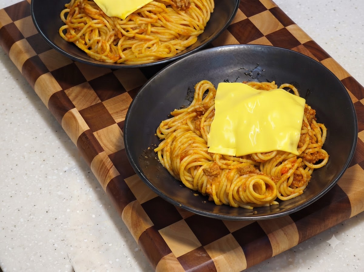 Plaster żółtego sera topiący się nad bazą ze spaghetti w czarnej misce do serwowania.