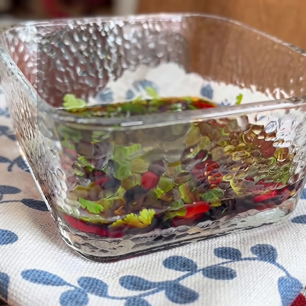 Zbliżenie na kwadratowe szklane naczynie wypełnione wytrawnym sosem z ziołami i papryczkami chili mieszanym za pomocą pałeczek.