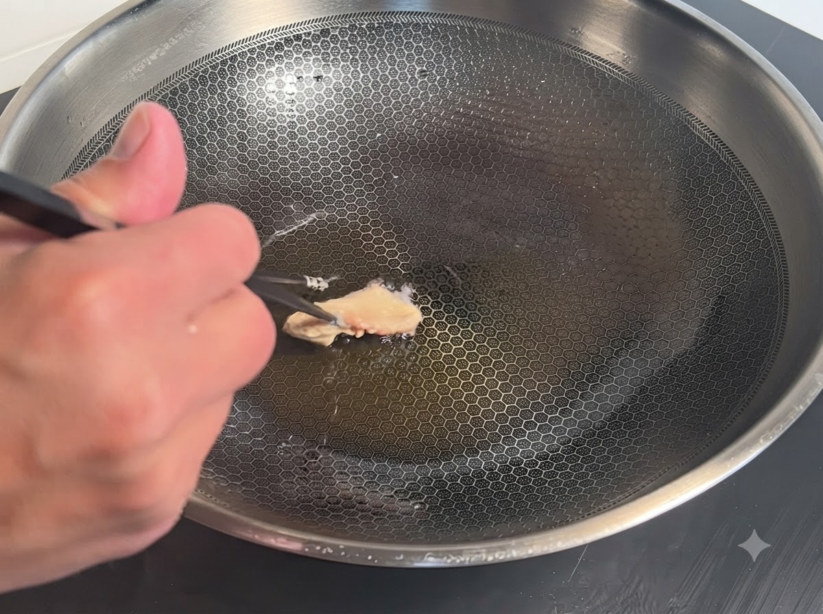 Pojedynczy kawałek kurczaka w panierce umieszczany pałeczkami na gorącej metalowej patelni wok z olejem.