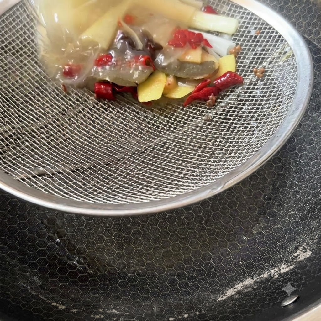 Sitko zatrzymujące pozostałe przyprawy, plastry imbiru i resztki chili nad pustym garnkiem.