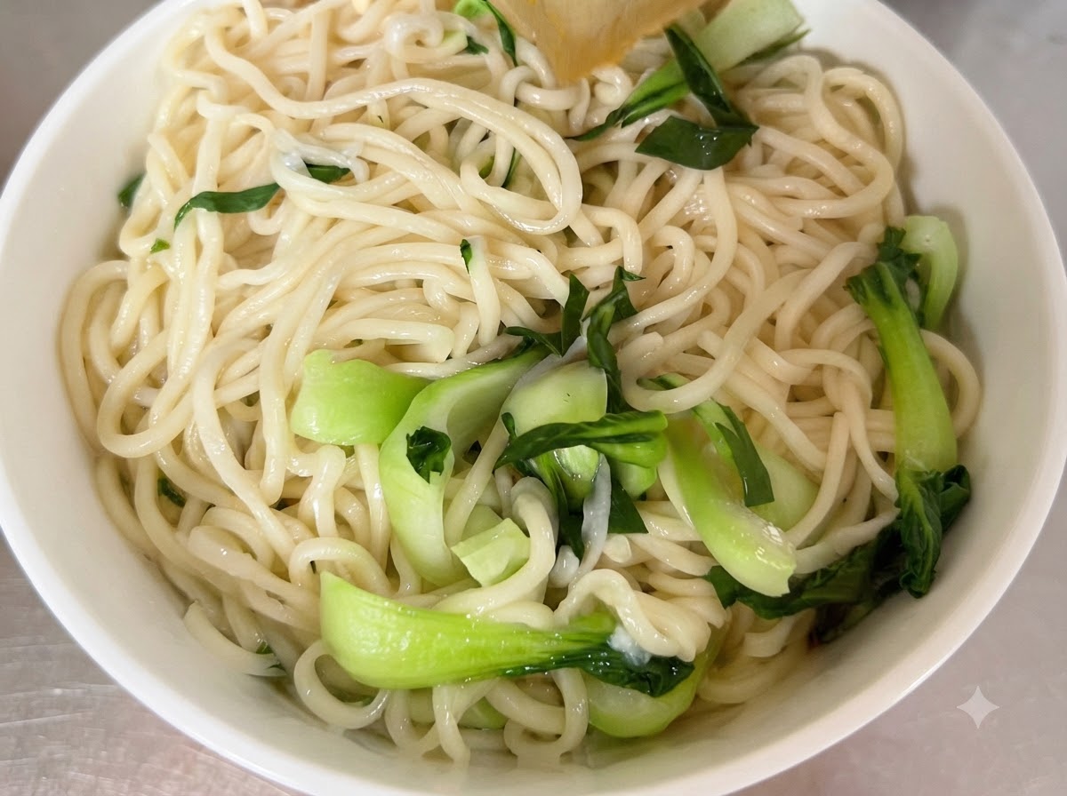 Ugotowany makaron i świeża kapusta bok choy ułożone w białej misce do serwowania.