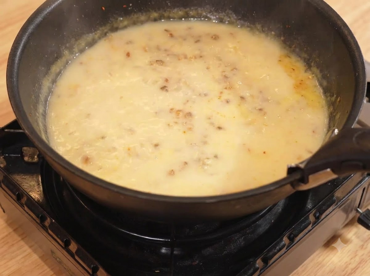 Woda i mleko wlewane na patelnię z mieszanką curry, gotujące się na małym ogniu.